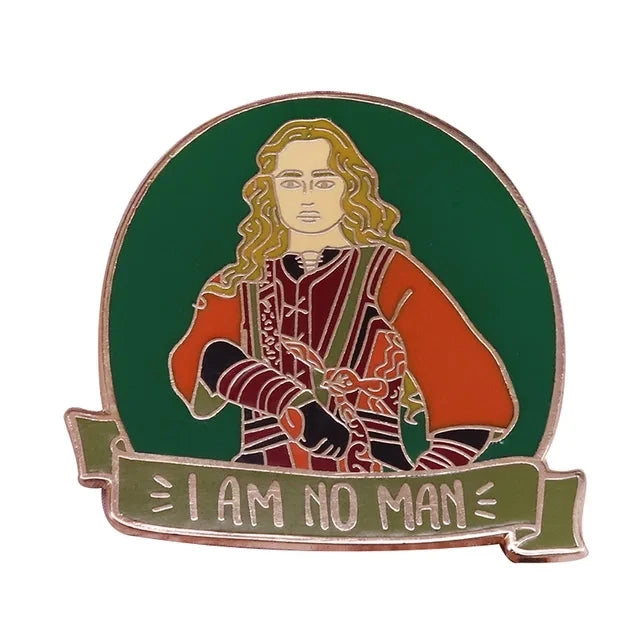 A green enamel pin featuring a depiction of a figure with long blonde hair and an orange garment, with the text I AM NO MAN b