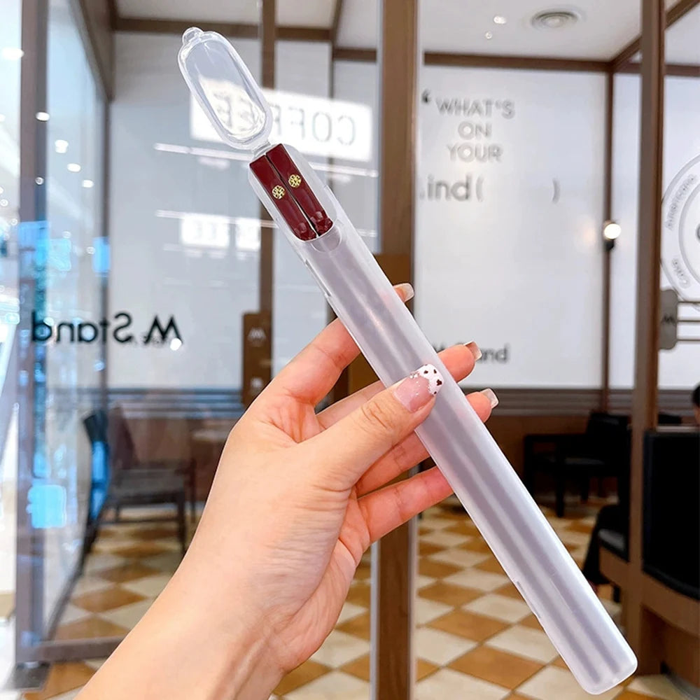 A hand holds a clear reusable Japanese and Korean chopsticks set with red tips against a blurred indoor background.
