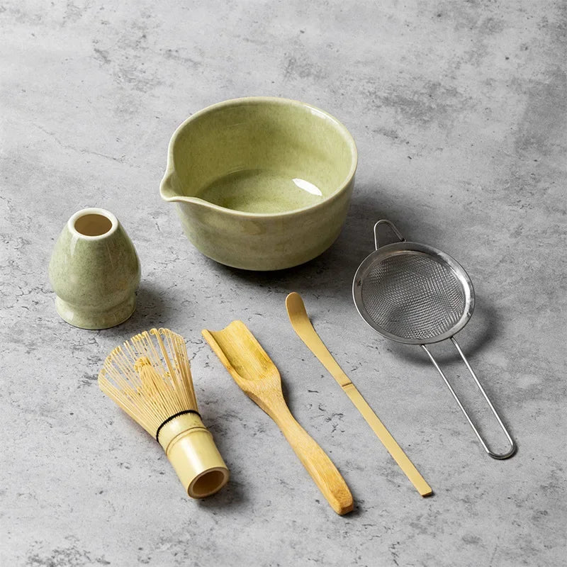 Un juego de herramientas para té matcha, incluyendo un cuenco de cerámica, colador y espátula de madera, sobre una superficie