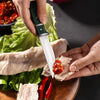 A hand is using a heavy-duty utility cleaver knife with a wooden handle to cut meat on a wooden board.