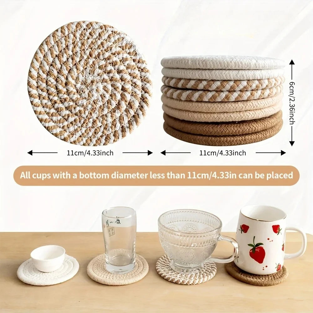 A set of four woven absorbent coasters in various shades of natural fiber are displayed on a wooden surface.