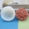 A white silicone flower candle mold and a pink silicone rose flower are displayed next to a book.