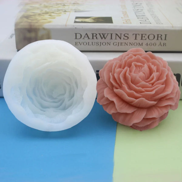 Eine weiße Silikonblumenkerzeform und eine rosa Silikonrosenblume werden neben einem Buch präsentiert.