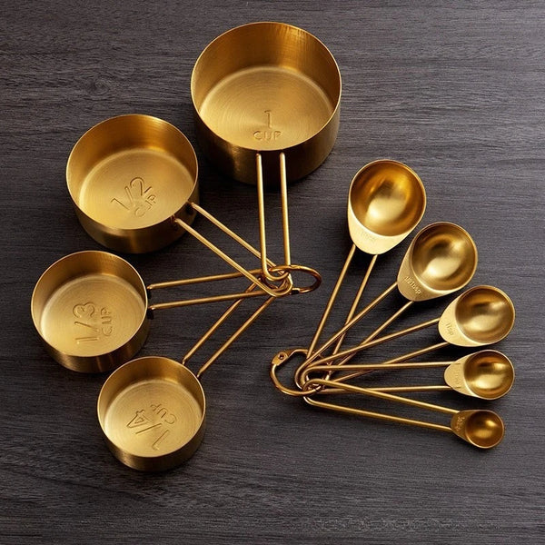 Ein Set aus Messing-Messbechern und -löffeln auf einer dunklen Oberfläche.