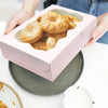 A person holds a pink decorative kraft paper candy box filled with round cookies on a gray plate.
