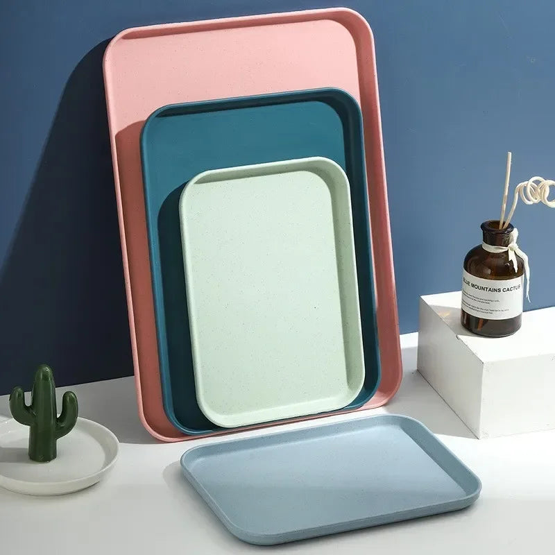 A stack of colorful plastic serving trays in pink, teal, and mint green against a dark blue wall.