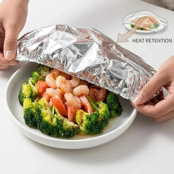 Hands open a reusable aluminum foil food cover revealing a serving of broccoli and shrimp for heat retention