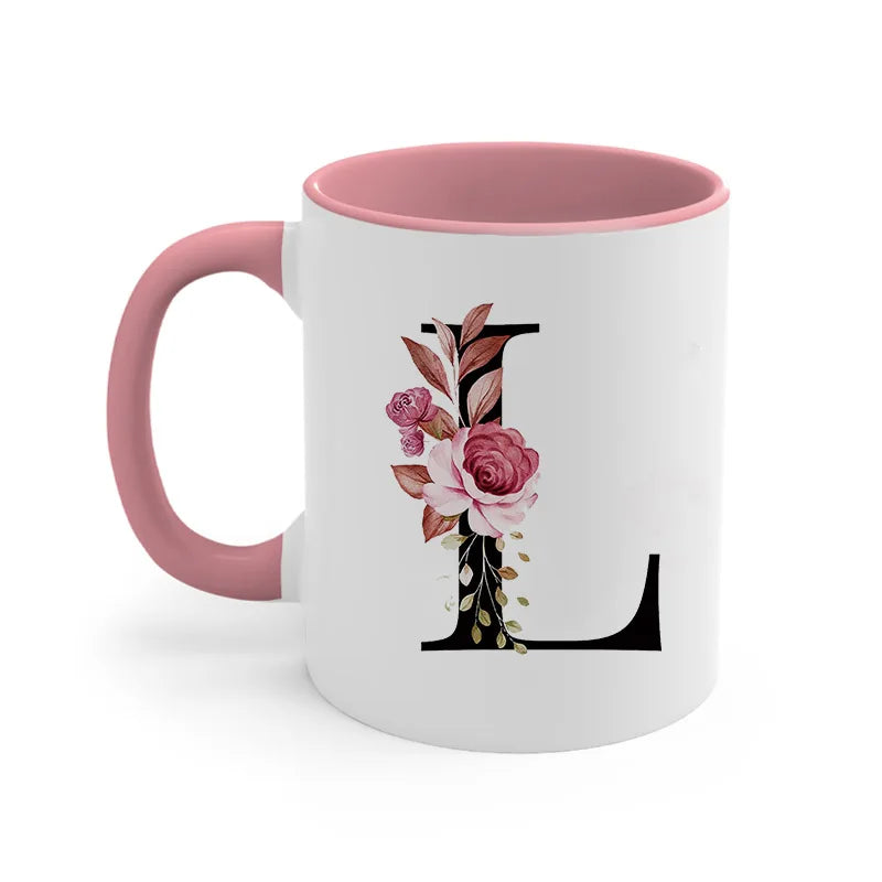A pink coffee mug with a black monogram design featuring a pink rose and green leaves.
