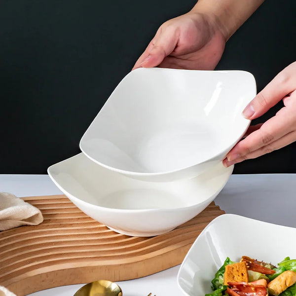Eine Hand hält eine weiße Salatschale über eine andere weiße Schale auf einem Holzbrett.