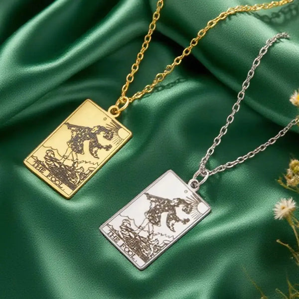 A gold and silver necklace featuring a tarot card pendant depicting a figure over a landscape on a green silk background.