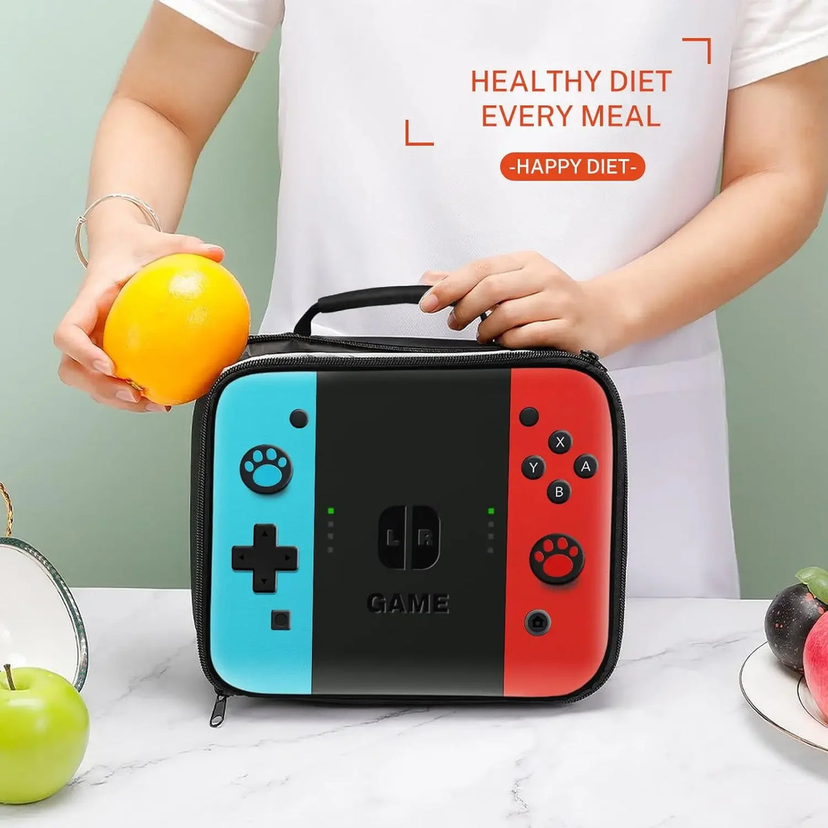 A black insulated thermal lunch bag with red and blue accents is held by a person, next to an orange and a green apple.