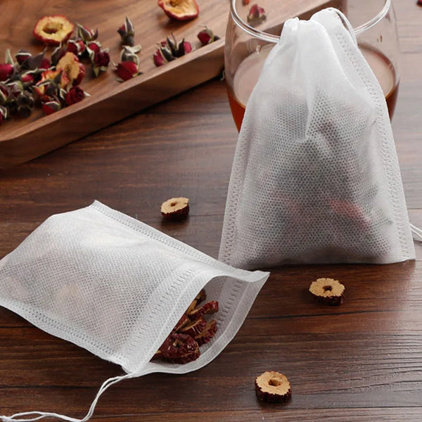 White disposable tea filter bags with drawstrings containing loose tea and spices on a wooden surface