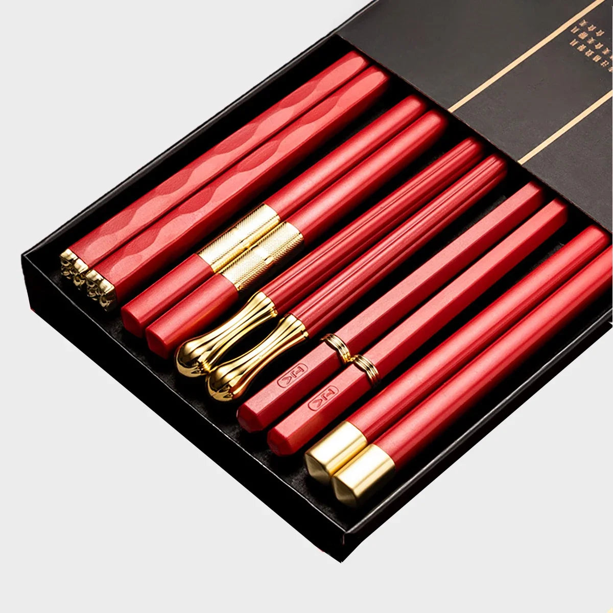 Un juego de palillos reutilizables de aleación rojo y dorado, exhibidos en una caja negra.
