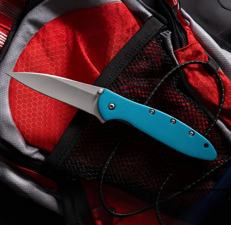 A silver utility knife with a blue handle is placed on a red and gray fabric background.
