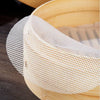 A white mesh silicone steamer liner is shown placed inside a bamboo steamer basket.