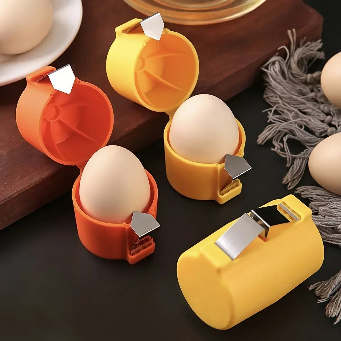 A set of orange and yellow portable tools for opening and separating egg shells, shown on a dark surface.