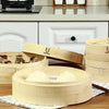 A set of light bamboo steamers and a wooden paddle are displayed on a table.