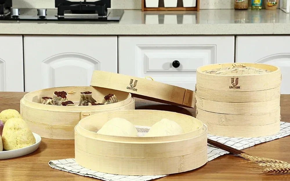 A set of light bamboo steamers and a wooden paddle are displayed on a table.