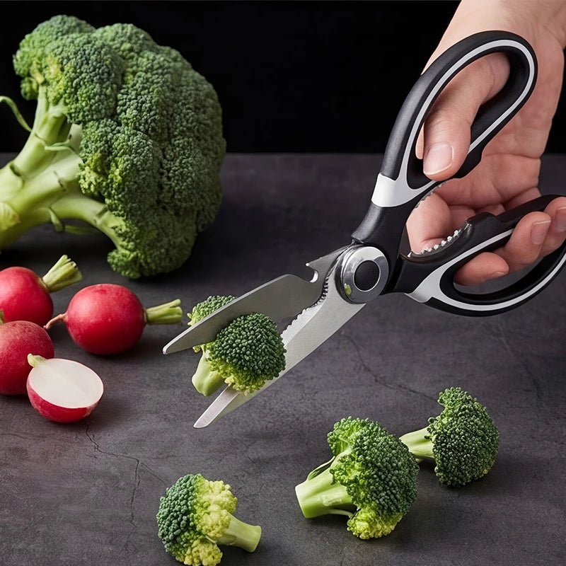 A hand uses professional stainless steel kitchen scissors to cut broccoli florets on a dark surface.