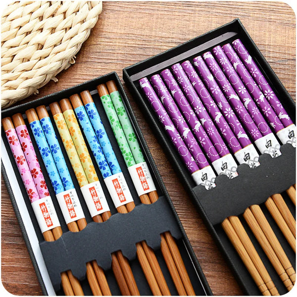 A set of natural bamboo chopsticks in various colors and designs are displayed in a black box.