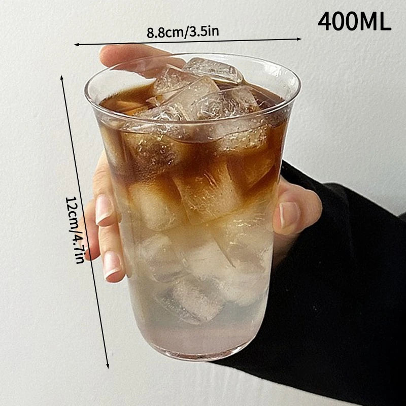 A hand holds a 400ml iced beverage in an elegant transparent glass tumbler with ice cubes.