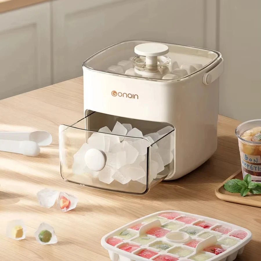 A white double-layer ice cube maker with a clear lid and a tray of ice cubes on a wooden surface.