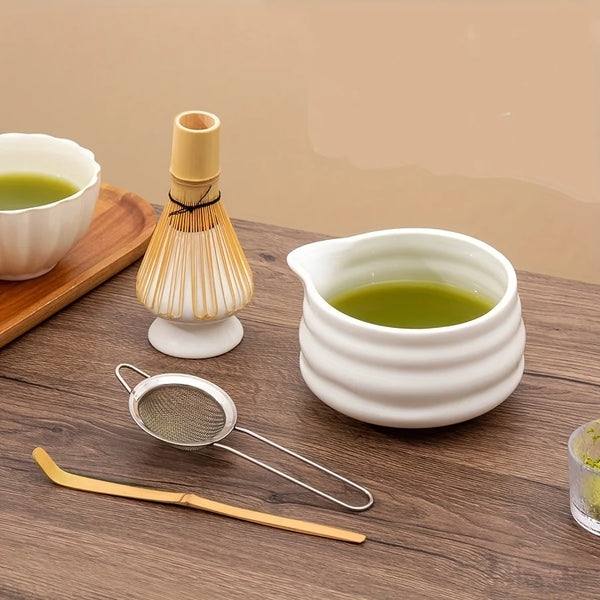 A set of five white ceramic matcha bowls and a bamboo whisk are displayed on a wooden surface.
