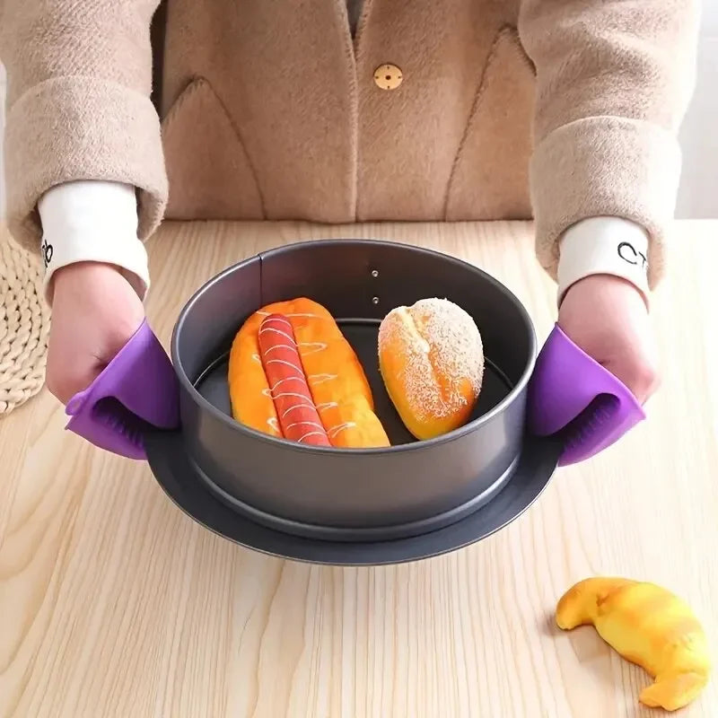 A person wearing purple silicone oven mitts holds a dark gray silicone baking dish containing two baked goods.