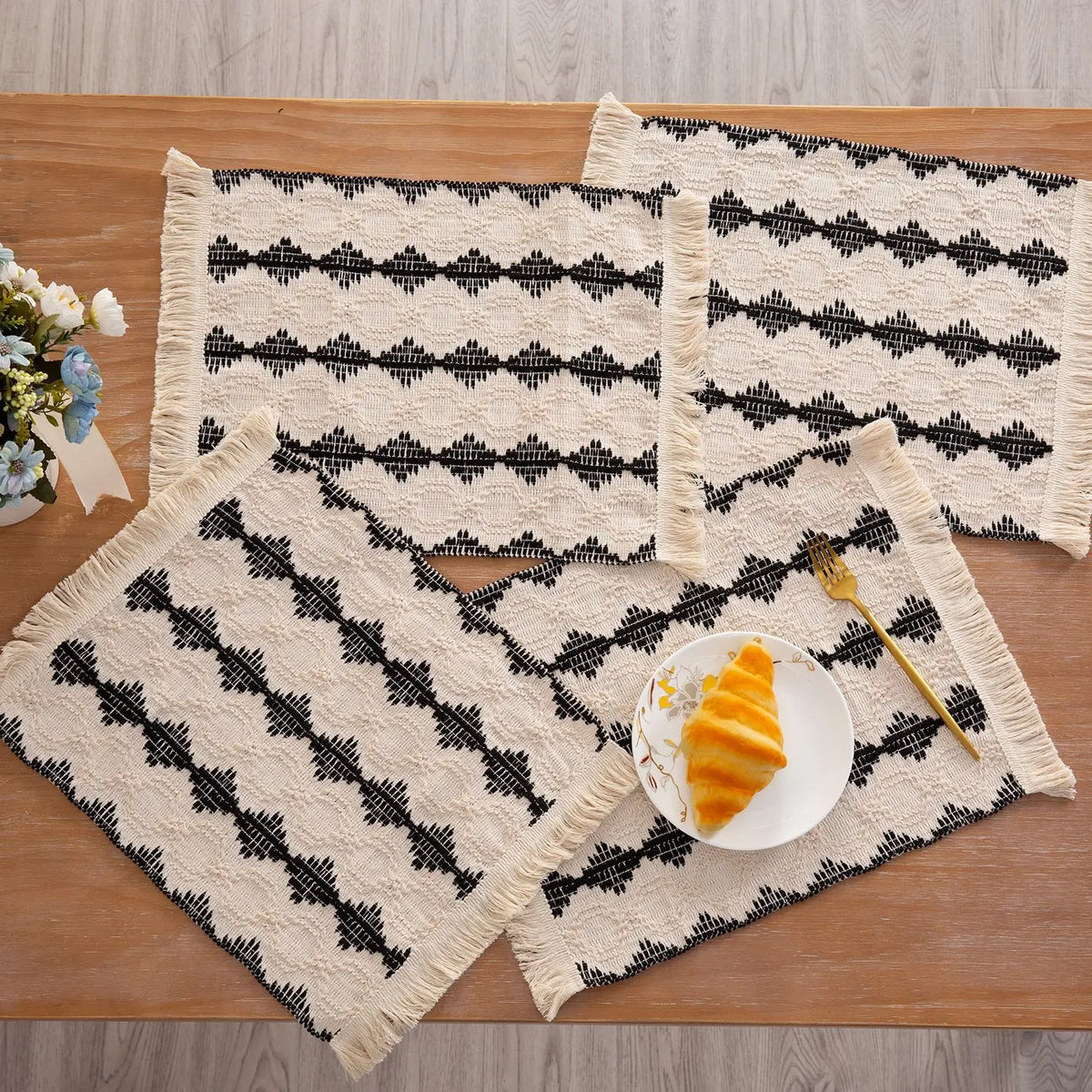 Ein Set aus schwarz-weiß gemusterten Jute-Platzsets mit Fransen auf einem Holztable