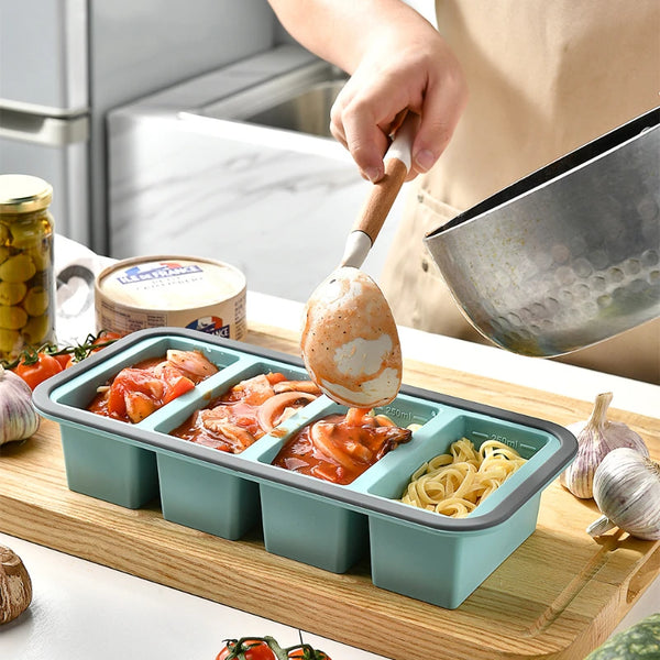 Silikon-Essgeschirr-Tabletts mit Deckeln, gefüllt mit gekochten Speisen wie Tomaten und Pasta auf einem Holzbrett
