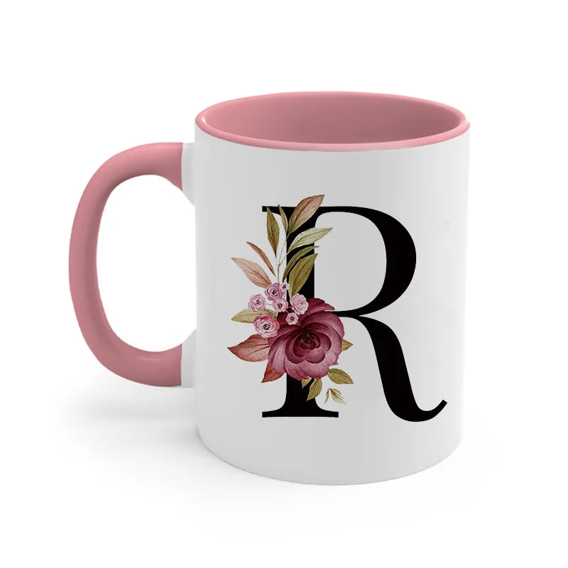 A pink ceramic coffee mug with a large black initial R decorated with floral elements.