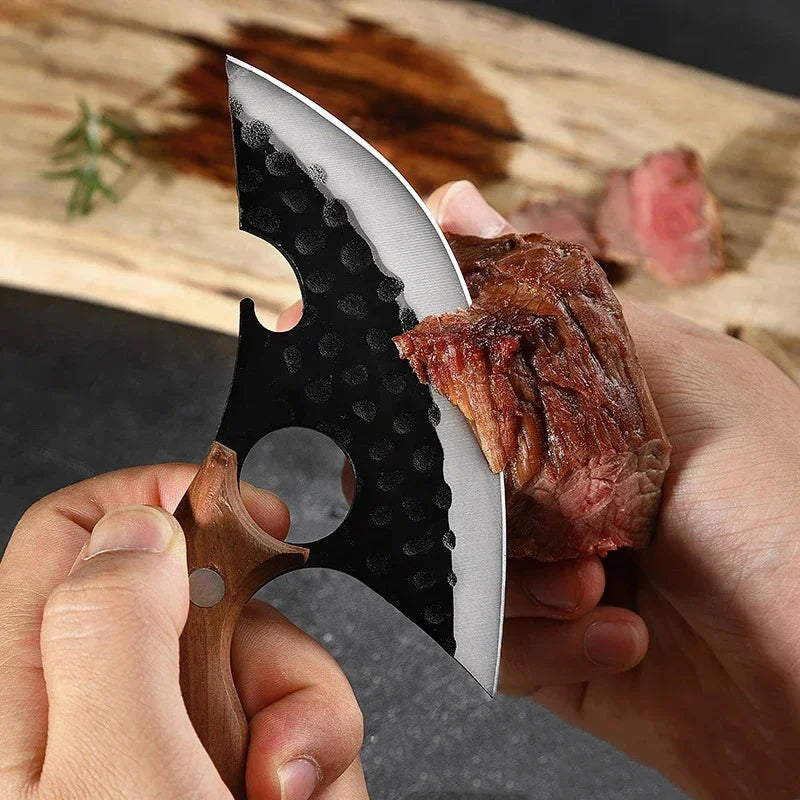 A hand holds a heavy-duty utility cleaver knife with a black blade and wooden handle, positioned next to a piece of cooked me