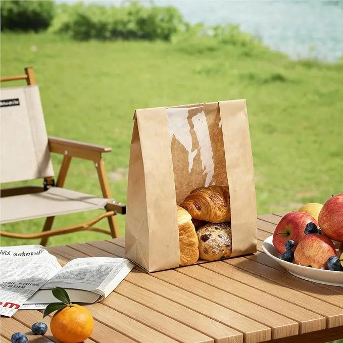 A set of kraft bakery bags with clear windows and seal stickers filled with baked goods on a wooden table.