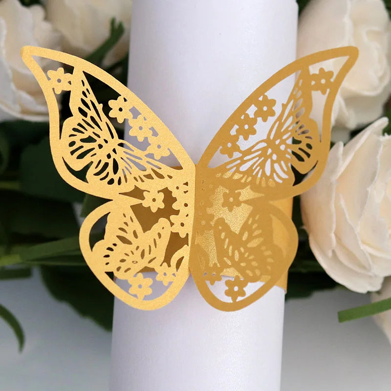 Gold laser cut butterfly napkin rings displayed against a white candle and cream roses.