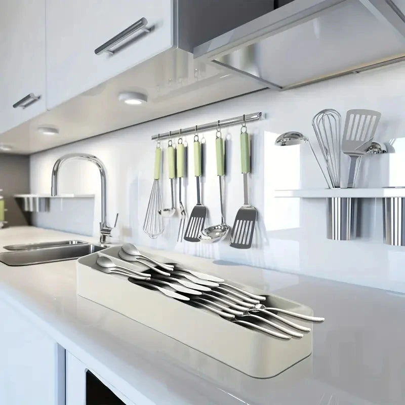Una encimera de cocina blanca con un organizador de cubiertos compartimentado lleno de cubiertos plateados.