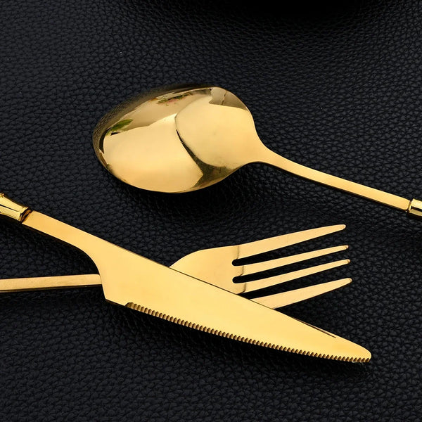 Set aus Edelstahlbesteck mit Goldakzenten, einschließlich Löffel und Gabel, auf dunkler Oberfläche.