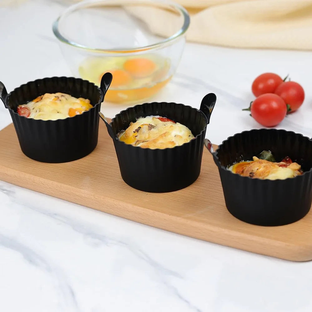 A set of four black reusable silicone egg poaching cups filled with scrambled eggs are displayed on a wooden board.