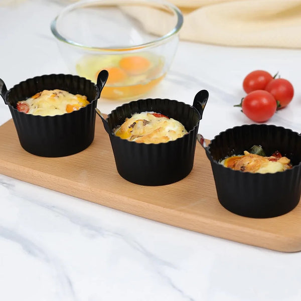 A set of four black reusable silicone egg poaching cups filled with scrambled eggs are displayed on a wooden board.
