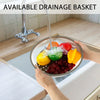 A hand is holding a glass bowl filled with fruit under a kitchen faucet, demonstrating an available drainage basket.