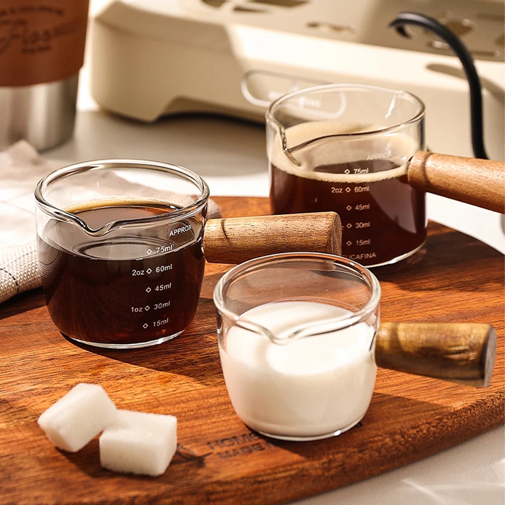Un juego de tazas medidoras de café de vidrio de precisión y una cuchara de madera sobre una tabla de cortar.