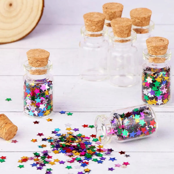 Klare Glasfläschchen gefüllt mit bunter Glitzer und mit Korkverschluss, verstreut auf weißer Fläche.