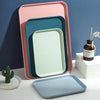 A stack of pink and teal plastic serving trays, including a large rectangular tray and a smaller square tray.