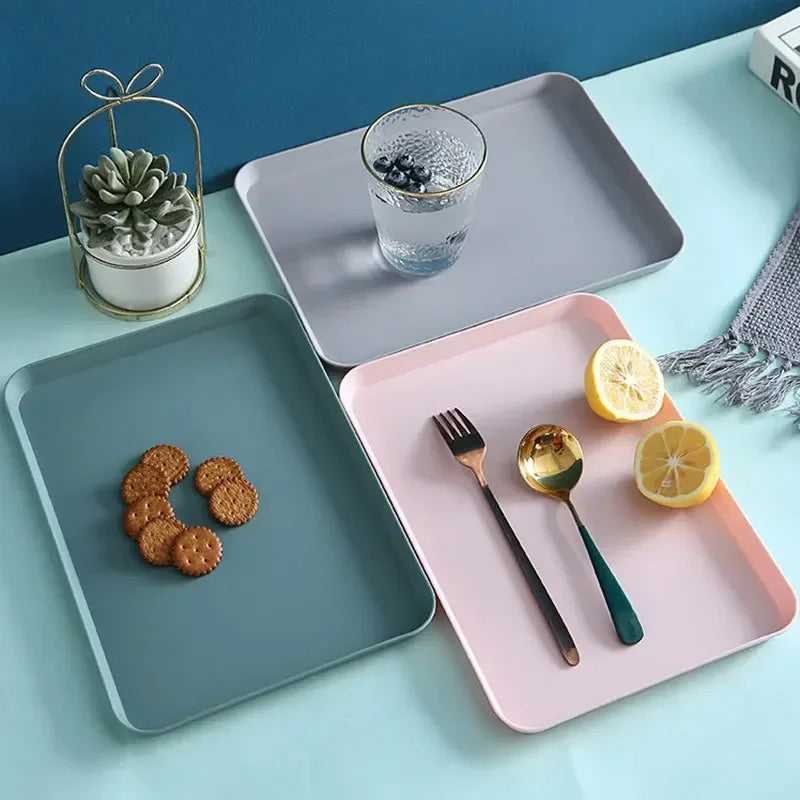 A pink serving tray holds cookies, a glass of water with berries, and slices of lemon on a light blue surface.