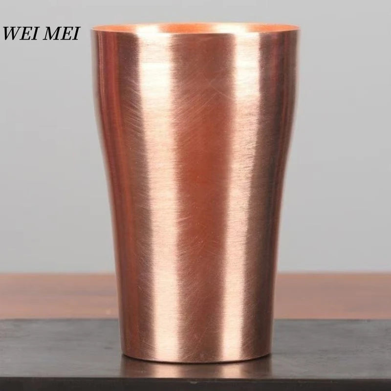 A tall, cylindrical copper coffee mug with a brushed finish sitting on a dark surface.
