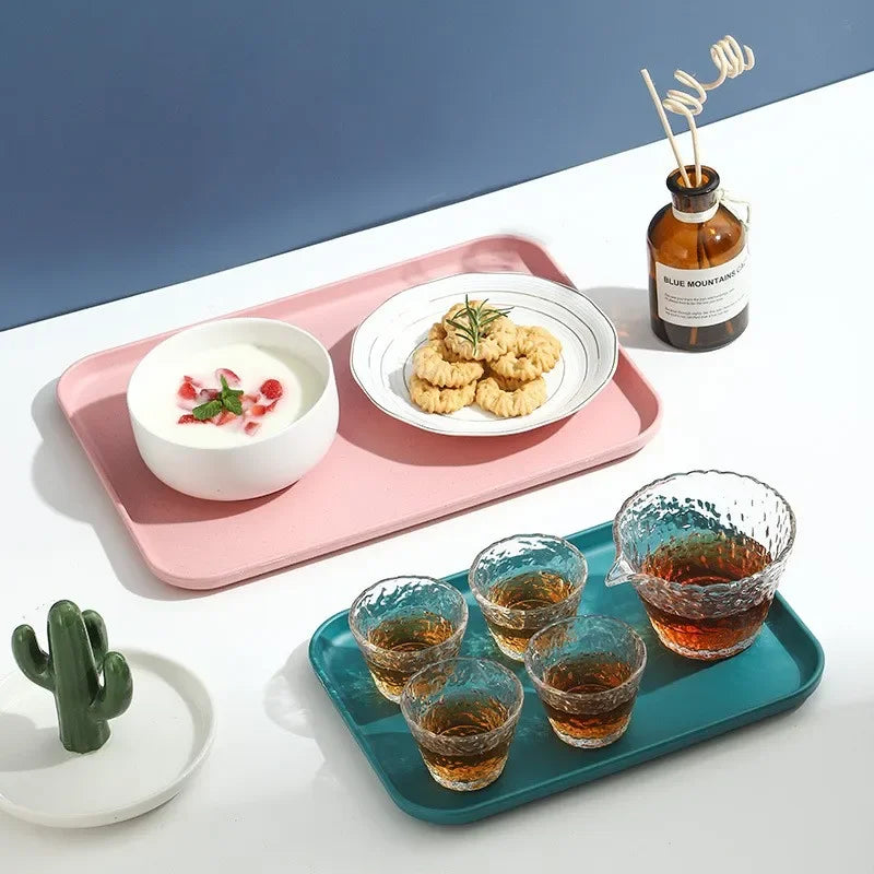 A pink serving tray holds a white bowl of cream and a plate of golden cookies, next to a glass bottle of blue mountain tea.