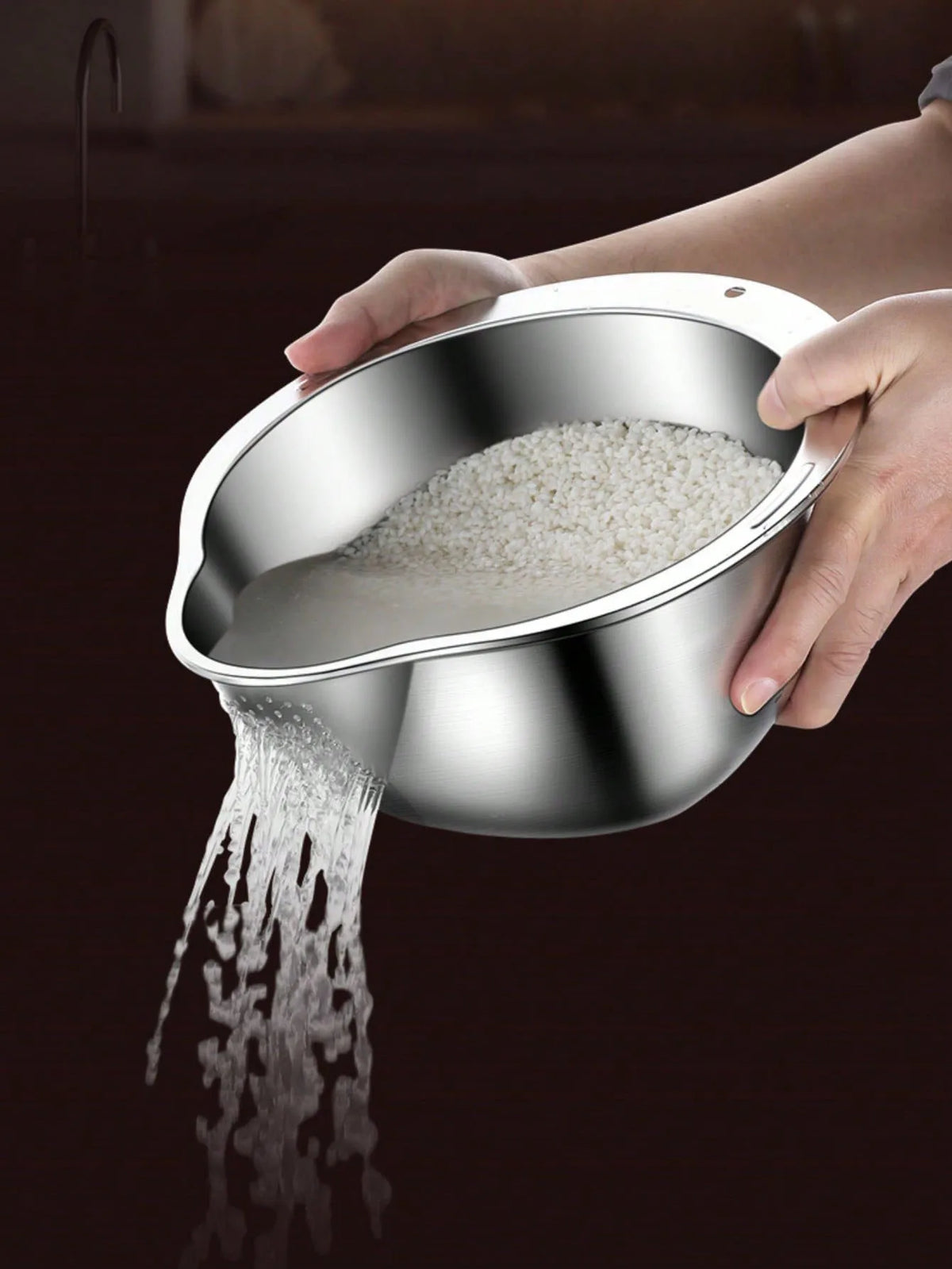 A hand is pouring white rice from a stainless steel bowl and strainer onto a surface.