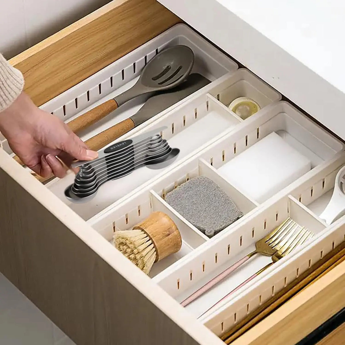 A magnetic stainless steel measuring spoons set is displayed in a white drawer organizer with wooden accents.