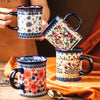 A hand holds a colorful bohemian floral ceramic mug, featuring blue, white, and pink patterns.