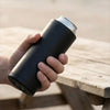A hand holds a black double tactical reload can holder on a wooden table.