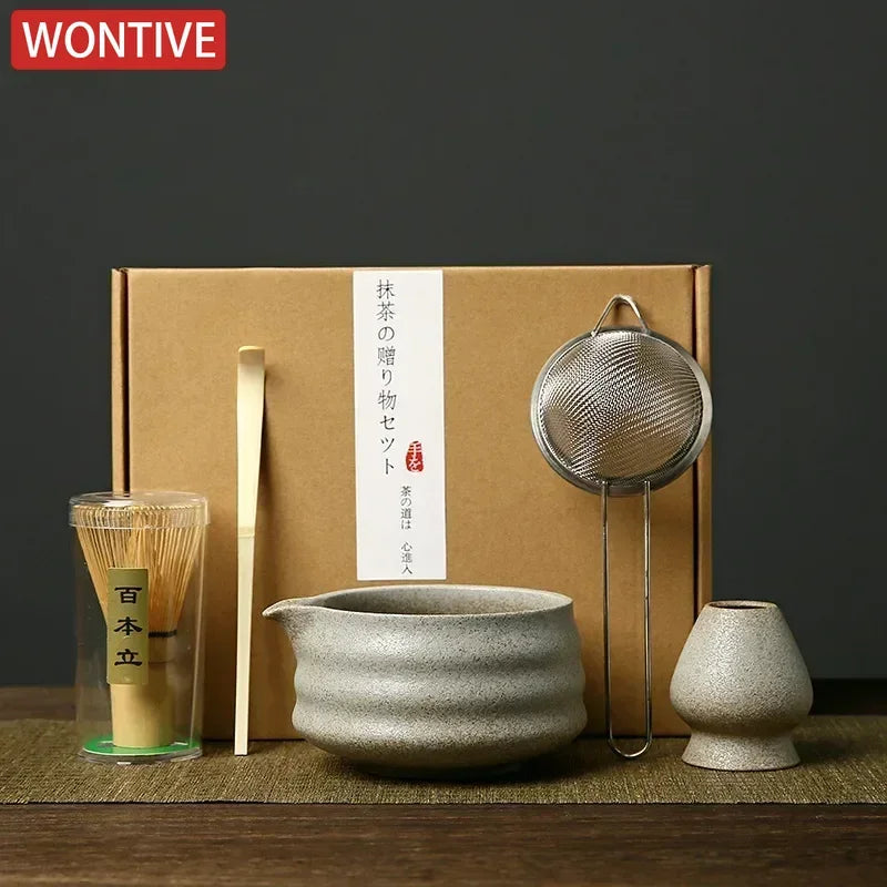A box containing a Japanese matcha whisk set, including bamboo whisks and a metal strainer, is displayed on a wooden surface.